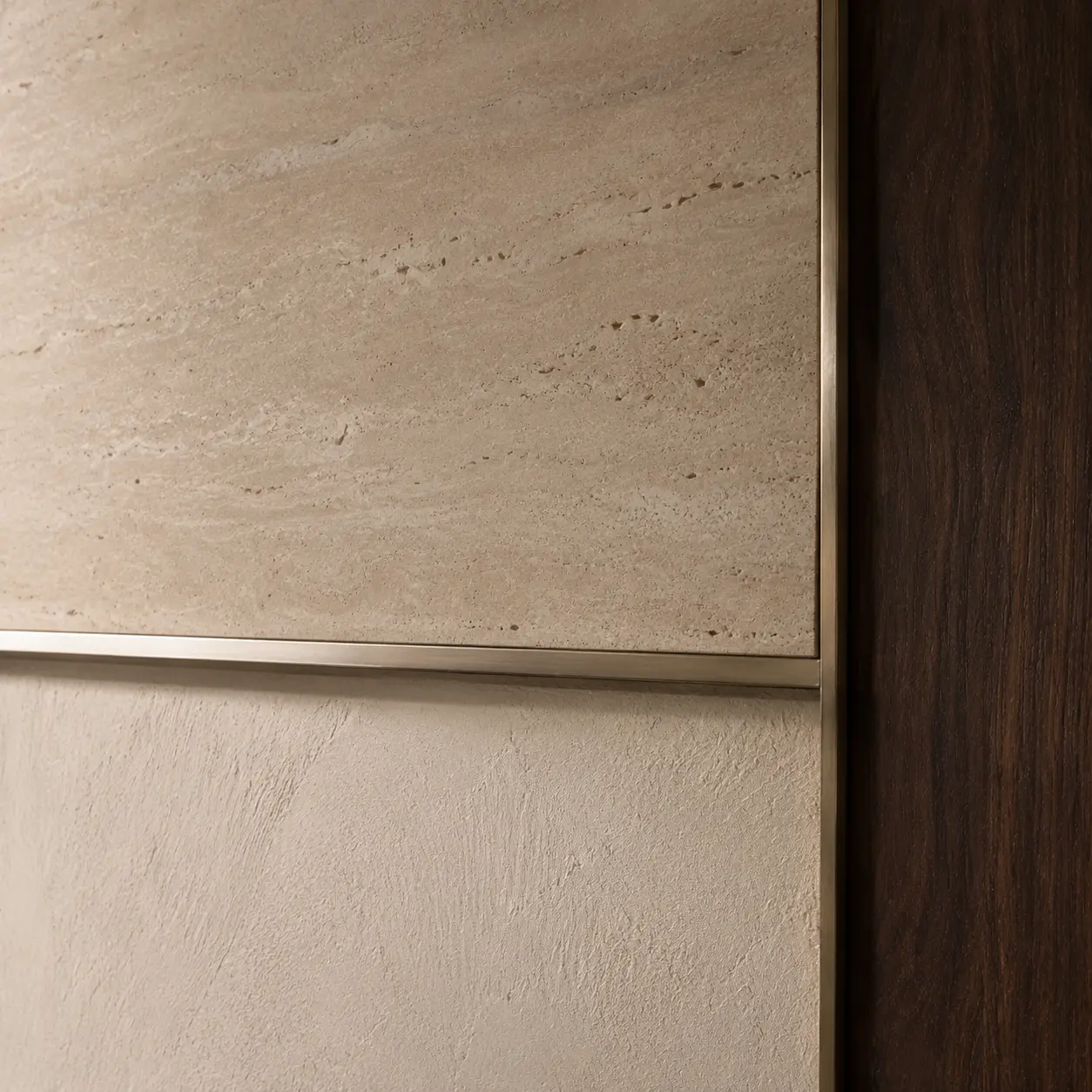 Close detail of travertine stone with a slim bronze trim against a textured plaster wall.