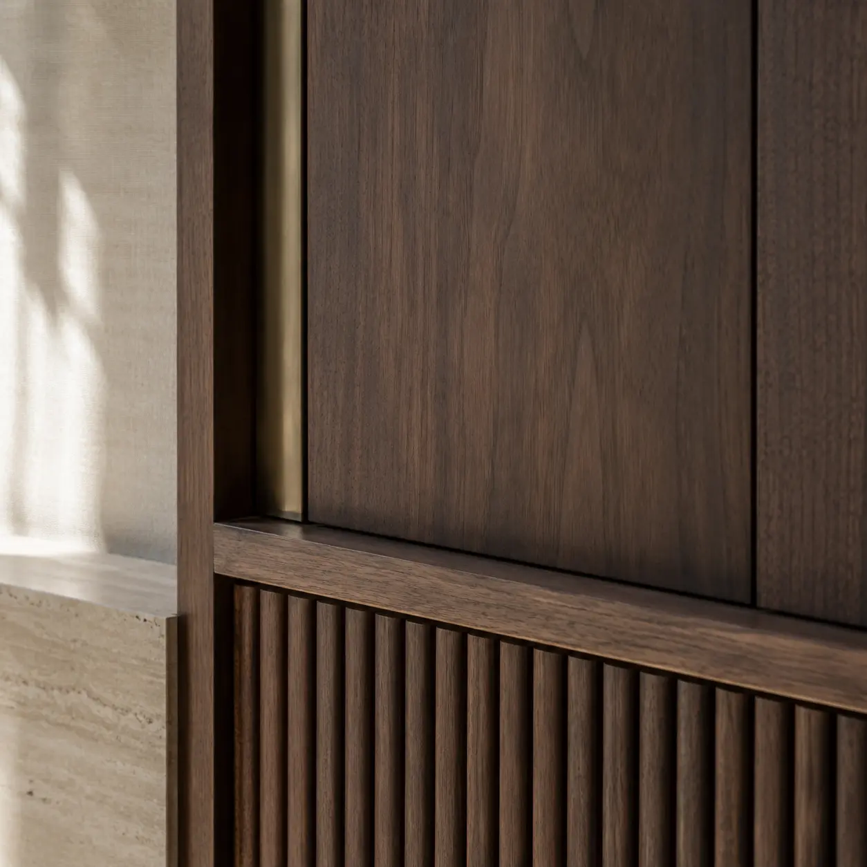 Close detail of walnut panelling with a fluted timber base and a thin brass reveal.